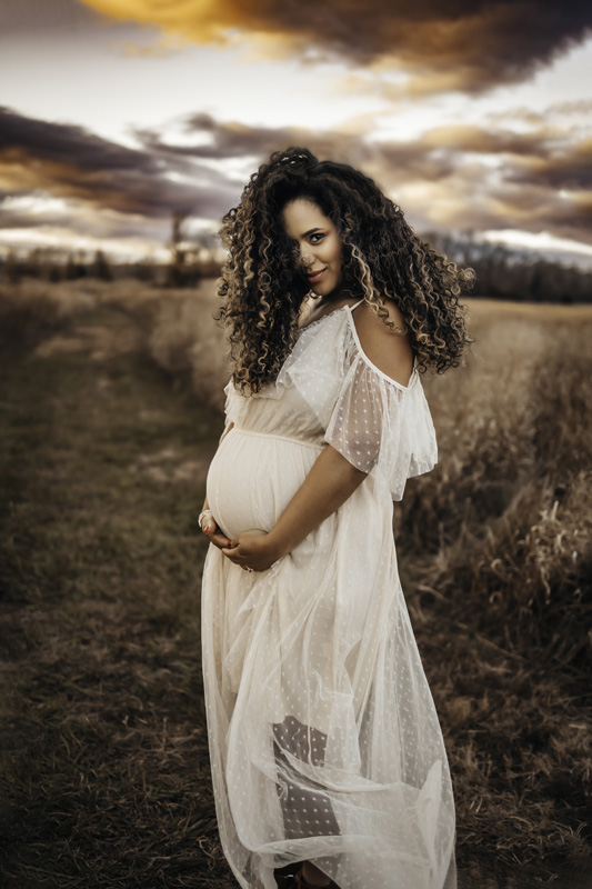 maternity photography, woman in white dress standing in a field holding her belly
