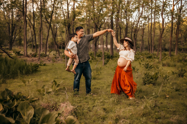 Family photography, Family of three dancing in a field with trees in the background