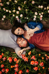 Family Photographer, husband and wife lay together in a bed of tulips